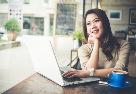 Young beautiful Asian woman working in coffee shop cafe, using computer laptop about business work and online shopping, smile and happy with copy space, vintage toneの写真素材