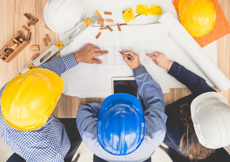 Group of engineers and architects discussing on table with drawing/blueprint, wearing safety helmet working for industrial construction and engineeringの写真素材