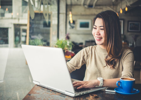Young beautiful Asian woman working in coffee shop cafe, using computer laptop about business work and online shopping, smile and happy with copy space, vintage toneの写真素材
