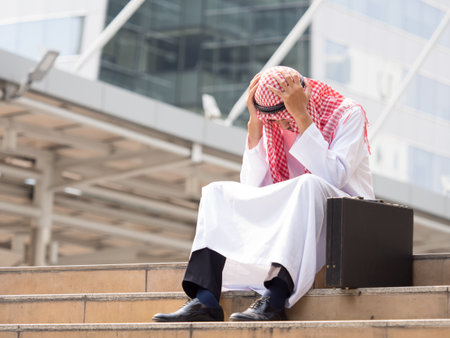 Upset arab businessman sitting at stairs in the modern city, holding head, feeling down, disappointed from business problem conceptの写真素材