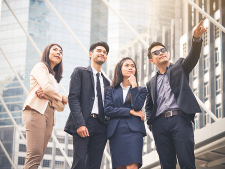 Group of young Asian businessman businesswoman 20-30s standing in the modern city, pointing out showing business plan in the futureの写真素材