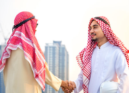 Handsome arab businessman, engineer/architect shaking hands front of building new construction project, togetherness, teamwork, cooperation for business conceptの写真素材