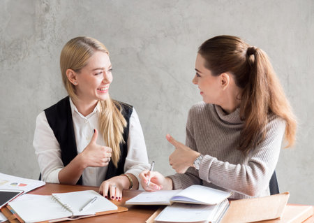 Two of young caucasian business woman working with happy feeling and smile in the office, sitting on desk with computer laptop reading good news and feeling surprise.の写真素材