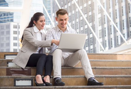 Businessman and businesswoman talking during working online on laptop at outdoor officeの写真素材