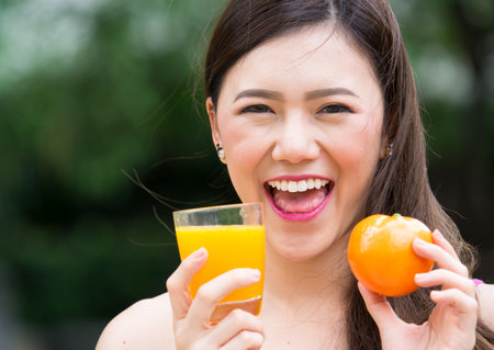 Young beautiful asian woman eating/drinking orange/orange juice fruits, healthy eating with clean food and fruit for diet contactの写真素材