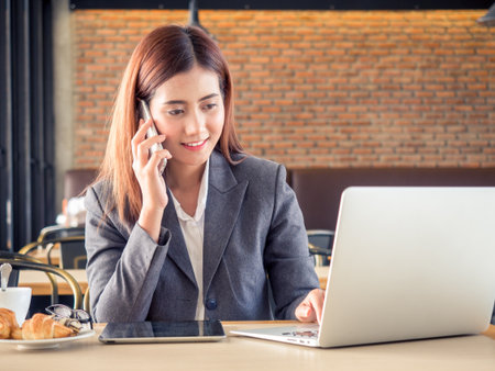 Young asian businesswoman talking on the phone during working with laptop on desk at cafeの写真素材