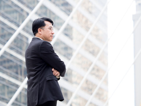 Portrait middle aged asian businessman in the city, businessman, manager, boss handsome looking with glasses crossed arms in the city concept.の写真素材