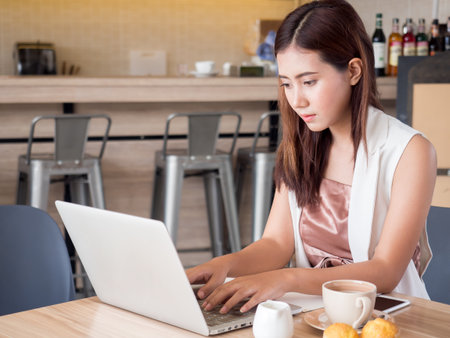 Young asian Businesswoman working, writing email on laptop, drinking coffee, doing shopping online at cafeの写真素材