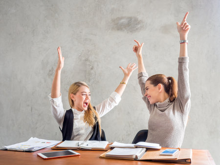Two businesswoman smile and raise hands up, feeling happy on Friday, complete finish job, successful/achievement working in office conceptの写真素材