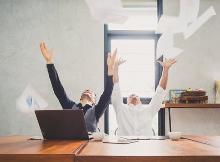 Two of young businessman trowing papers papers/sheets for work after finishing work, successful in business target in modern office, feeling happy, cheerful and relaxの写真素材
