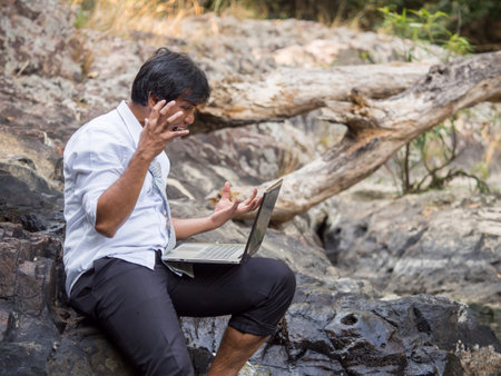 Middle age asian businessman in casual suit working in nature forest with crazy/mad/angry/stressed/serious feeling, working with laptop computer, business in forest/park/outdoor crazy feeling conceptの写真素材