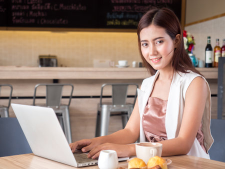 Young asian Businesswoman working, writing email on laptop, drinking coffee, doing shopping online at cafeの写真素材