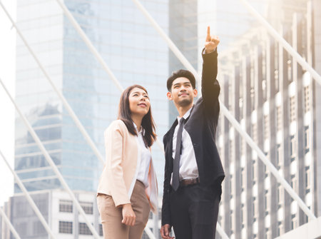 two of young asian businessman businesswoman 20-30s standing in the modern city, pointing out showing business plan in the futureの写真素材