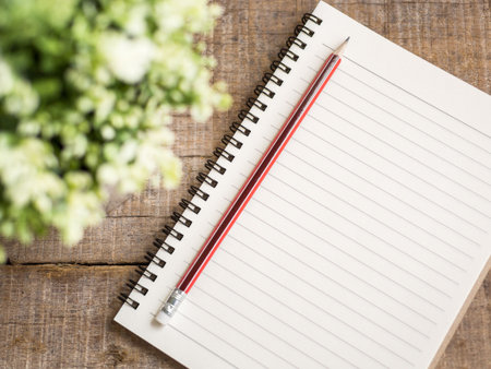 Soft focus pencil and notebook on wooden blur background with flowersの写真素材