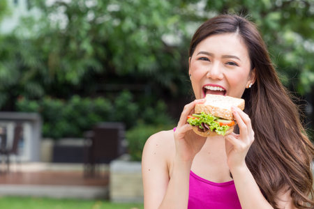 Young beautiful asian woman eating fresh clean food sandwich with vegetables and fruits for good healthy over green background, healthy food woman for dietの写真素材