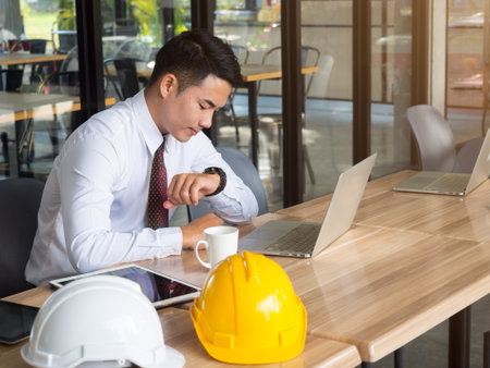 Asian engineer watching on his watch during working  by laptop in cafe, punctual/rush hour/dead line conceptの写真素材