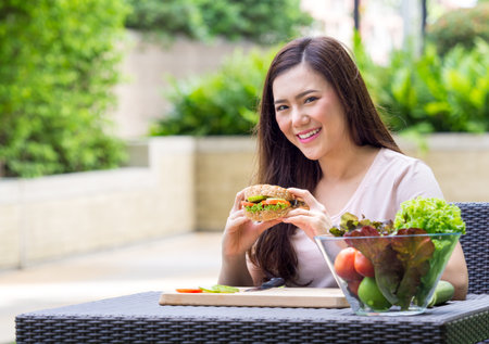 Young beautiful asian woman eating fresh clean food sandwich with vegetables and fruits for good healthy over green background, healthy food woman for dietの写真素材