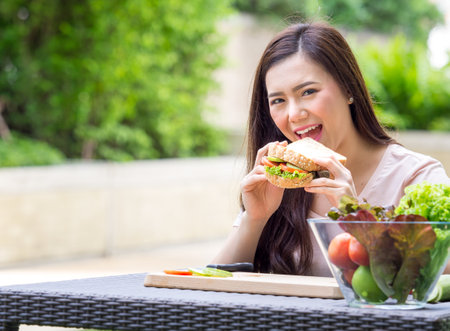Young beautiful asian woman eating fresh clean food sandwich with vegetables and fruits for good healthy over green background, healthy food woman for dietの写真素材