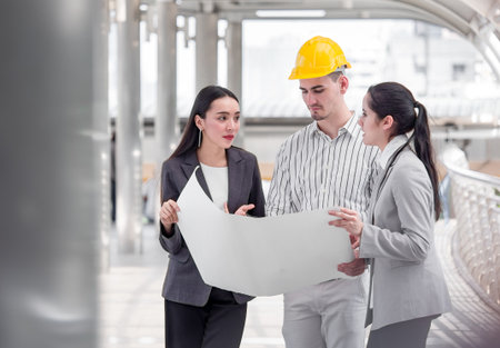 Young caucasian engineer/architect holding drawing/blueprint discuss with businesswoman for a project construction city building, happy feeling, positive, teamwork and togetherness conceptの写真素材