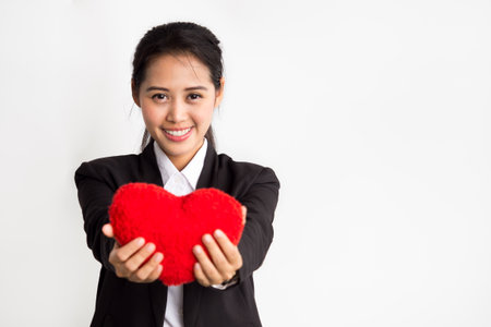 Young asian businesswoman holding red heart on white background, love and teamwork in working place office conceptの写真素材