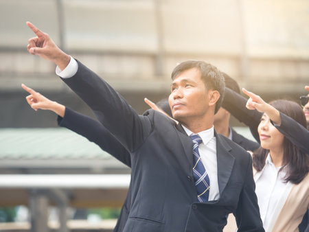 Group of young Asian businessman businesswoman 20-30s standing in the modern city, pointing out showing business plan in the futureの写真素材
