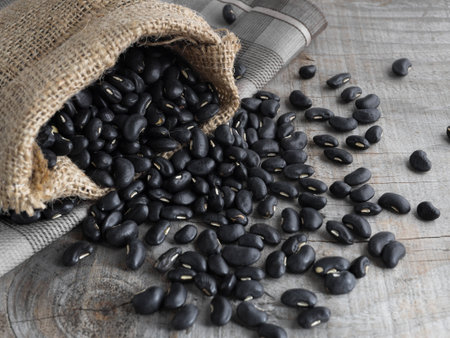 Black beans in a sack, black beans in a wooden bowl on a black wooden background.の写真素材