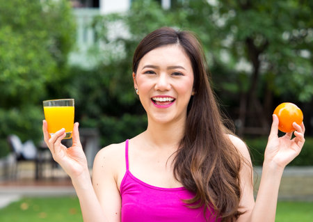 Young beautiful asian woman eating/drinking orange/orange juice fruits, healthy eating with clean food and fruit for diet contactの写真素材