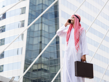 Portrait young arabian businessman holding bag and talking on the phone in the modern city, feeling smart, happy and successful conceptの写真素材