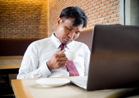 Middle age Asian businessman feeling sleepy during working on laptop and meeting at cafÃ© officeの写真素材