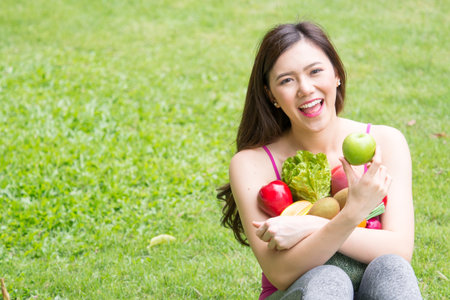 Young beautiful asian woman holding fresh clean food with vegetables and fruits for good healthy over green background, healthy food woman for dietの写真素材