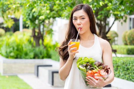 Young beautiful asian woman eating fresh clean food with vegetables/orange juice and many fruits for good healthy over green background, healthy food woman for dietの写真素材