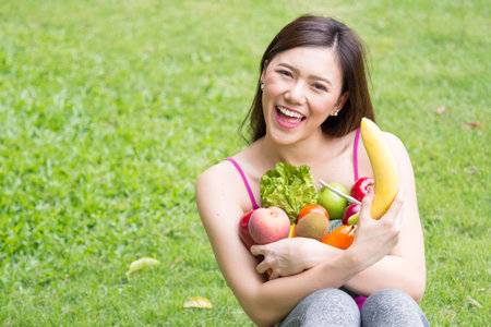 Young beautiful asian woman holding fresh clean food with vegetables and fruits for good healthy over green background, healthy food woman for dietの写真素材