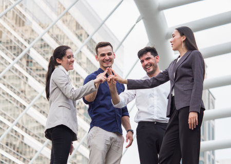 young businessman and businesswoman express teamwork, stacking hands at outdoor officeの写真素材