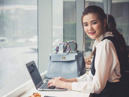 Young asian businesswoman working on laptop at coffee shop cafe during raining, smiling and happy working.の写真素材