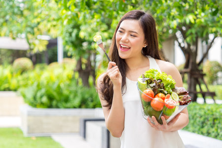 Young beautiful asian woman eating fresh clean food with cucumber vegetables and fruits for good healthy over green background, healthy food woman for dietの写真素材