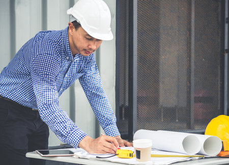 Engineer/architect/worker man discussing about building plan for construction at job site, working on desk/table with drawing/blueprint/business planの写真素材
