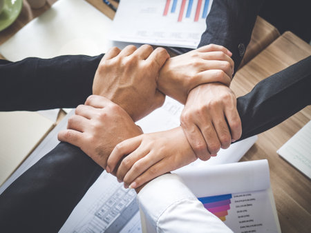 stacking hands of businessman and businesswoman while meeting at office over the meeting desk/table, teamwork, togetherness and business cooperation conceptの写真素材