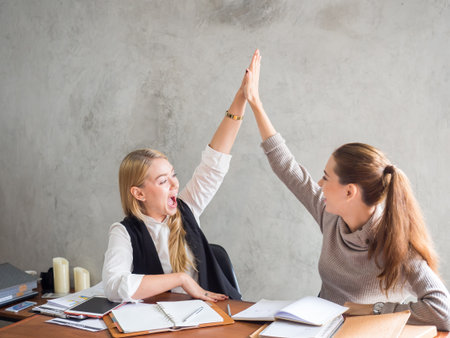 Two businesswoman smile and raise hands up, feeling happy on Friday, complete finish job, successful/achievement working in office conceptの写真素材