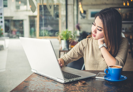 Young beautiful Asian woman working in coffee shop cafe, using computer laptop about business work and online shopping, smile and happy with copy space, vintage toneの写真素材