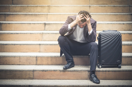 Upset young caucasian businessman tired from work sitting at stairs, unemployment, fired from job, disappointed, loss and feeling down conceptの写真素材
