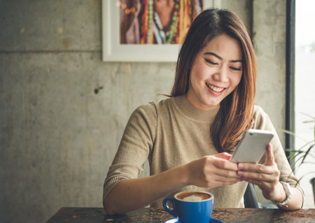 Young Asian beautiful woman using smart phone for business, online shopping, transfer money, financial, internet banking. in coffee shop cafe over blurred background.の写真素材