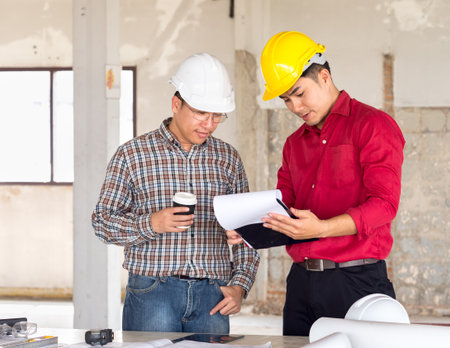 Engineer/architect/worker man discussing about building plan for construction at job site, working on desk/table with drawing/blueprint/business planの写真素材