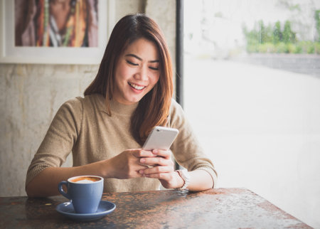 Young Asian beautiful woman using smart phone for business, online shopping, transfer money, financial, internet banking. in coffee shop cafe over blurred background.の写真素材