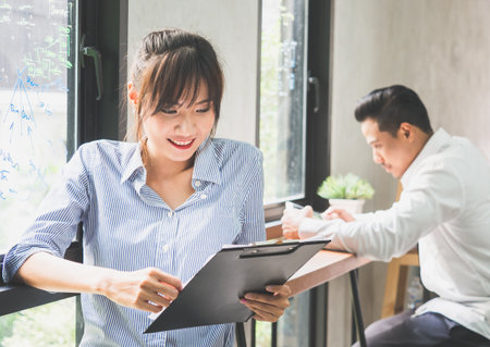 Young beautiful asian woman reading financial documents report over businessman in cafe officeの写真素材
