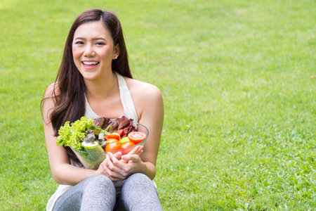 Young beautiful asian woman holding fresh clean food with vegetables and fruits for good healthy over green background, healthy food woman for dietの写真素材