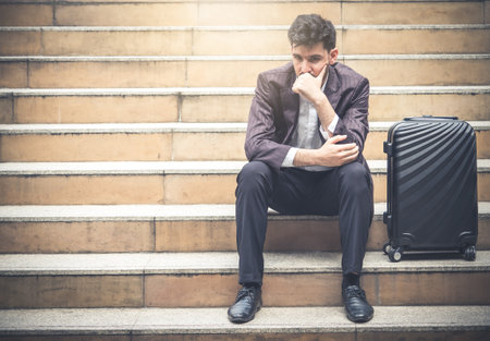 Upset young caucasian businessman tired from work sitting at stairs, unemployment, fired from job, disappointed, loss and feeling down conceptの写真素材