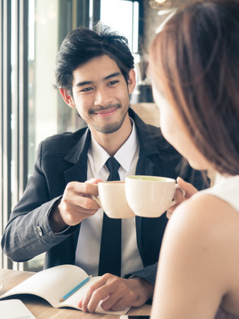Two of young businessman / woman in casual suit talking and drinking coffee during meeting at cafeの写真素材