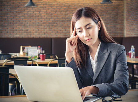 Young asian businesswoman thinking/doubt/questioning during working with laptop at cafeの写真素材