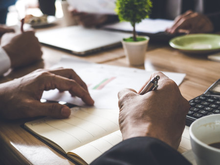 Meeting table, desk, businessman takes note during meeting for business plan, strategy, financial report and status, coffee and many documents on the table while discussing.の写真素材