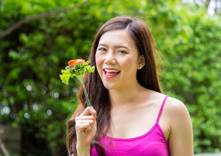 Young beautiful asian woman eating fresh clean food with vegetables and fruits for good healthy over green background, healthy food woman for dietの写真素材